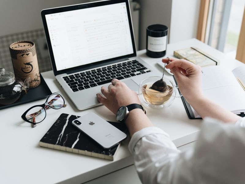 A person in a white shirt works at a laptop on a bright white desk, one hand resting on the trackpad while the